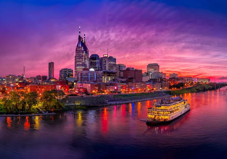 Waterfront view of downtown Nashville, TN skyline at dusk with riverboat in foreground.