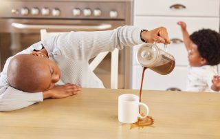 Tired parent spilling coffee as energetic child plays in the background